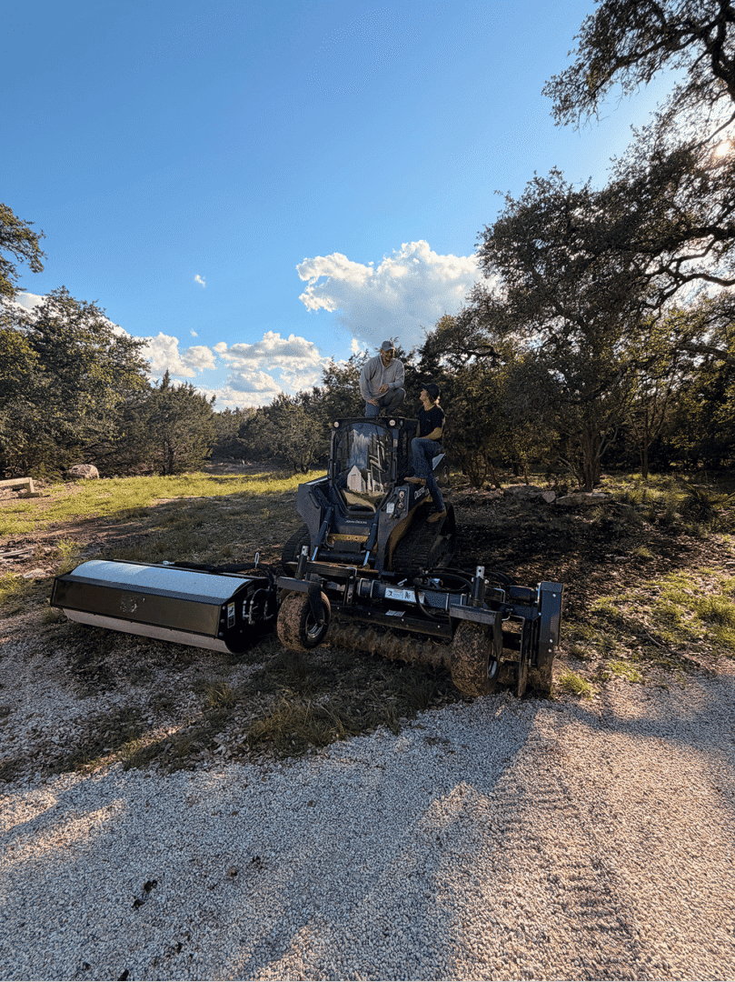 Two men atop compact earth-moving machine